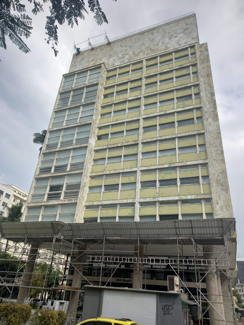 Edificação com andaime, proteção de calçada e equipe em intervenção na fachada.